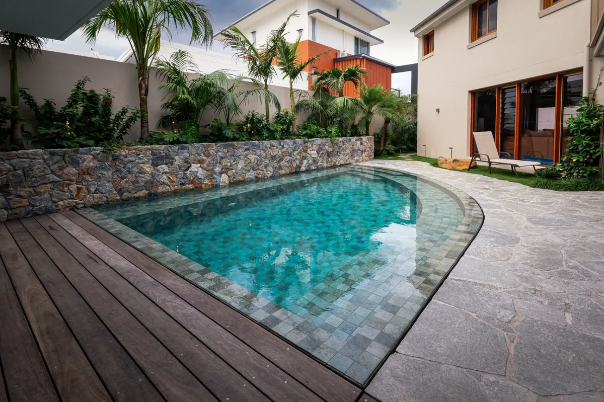 Green mosaic tiled concrete pool with stone wall and timber deck, Tugun
